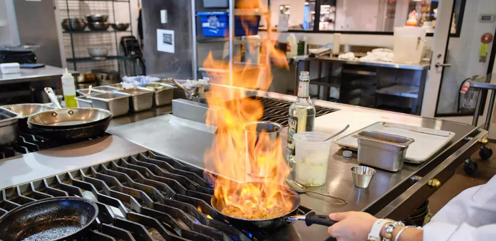 A chef cooks with a pan on fire