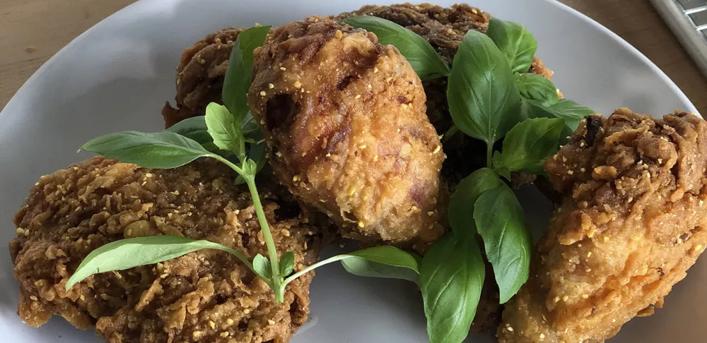 Three pieces of buttermilk lemonade fried chicken garnished with whole basil leaves sit on a white plate