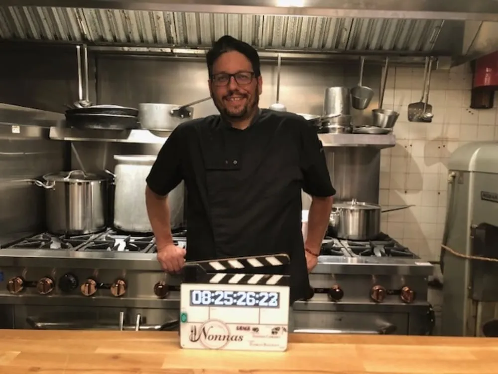 ICE alum Chef Jason Forella stands behind kitchen counter as food stylist on set of "Nonnas" on Netflix