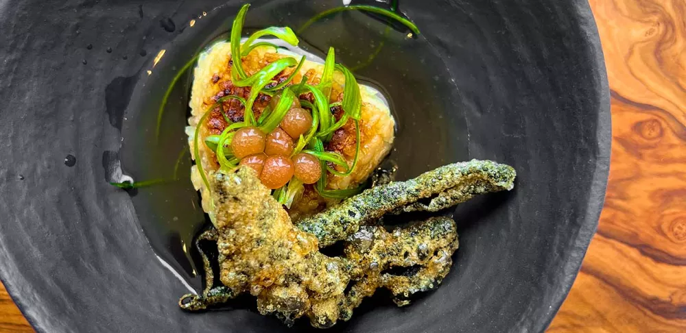 A piece of onigiri and multiple pieces of plant-based "salmon" skin sit on a blue plate