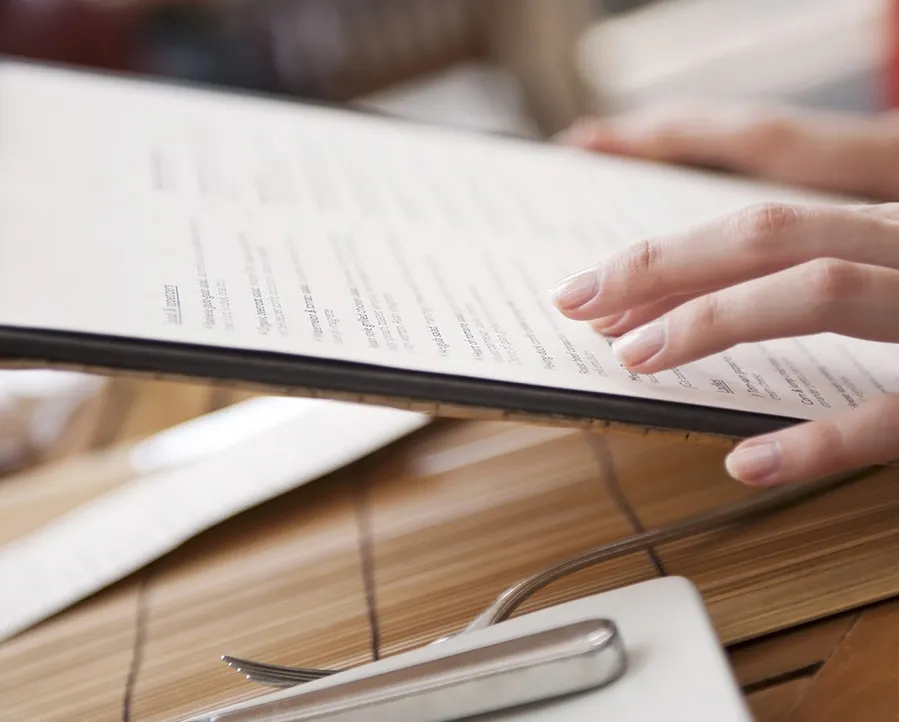 Close up image of a restaurant menu with a guest's hand scrolling the items.