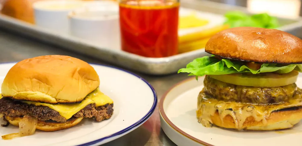 A smash burger and a restaurant-style burger sit next to each other on white plates