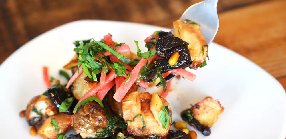 Sunchokes, also known as jerusalem artichokes, are used in a jerusalem artichoke recipe mixed with green herbs, olives and parsnips on a white plate on a wooden table