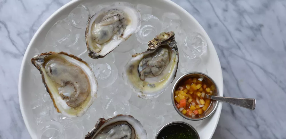 Oysters sit in an ice bucket with a sauce to the side for a valentine's day meal