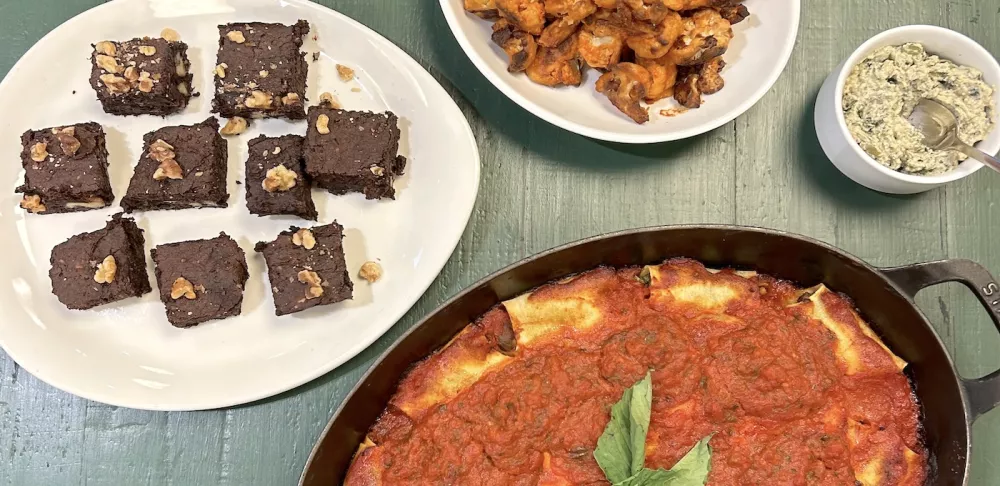 Vegan lasagna roll ups, buffalo cauliflower florets, pumpkin seed dip and brownies sit on a green table