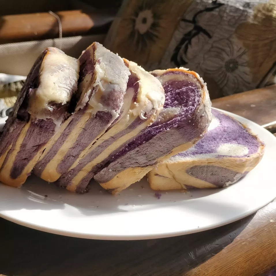 5 thick slices of purple swirled ube bread sit on a white plate.