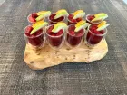 A wooden tray holds six glasses filled with assorted fresh fruits, showcasing vibrant colors and textures.
