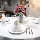 A set table with white tablecloth and red flowers in a vase