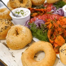 Bagels sit next to a variety of colorful toppings and cream cheese on a white table