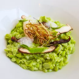 Green edamame risotto topped with mushrooms and fried leeks sits in a white plate