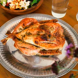 A roast turkey with herbs on top sits on a silver platter on a wooden table