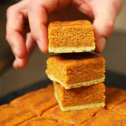 a hand places an orange pumpkin blondie bar on a stack of blondies