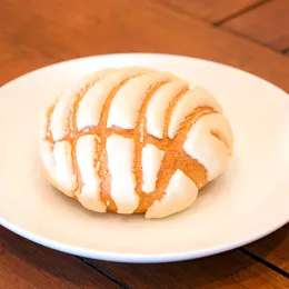 A concha pastry with a white cracked topping on a white plate