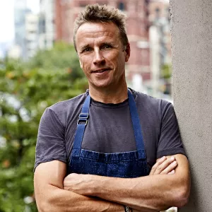 Chef Marc Murphy, a blonde man with a grey shirt and a blue apron, smiles