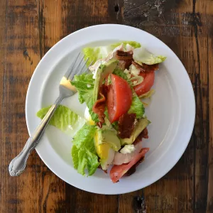 Cobb salad with sliced tomatoes, hard boiled eggs and salad greens sits on a white plate