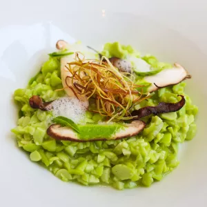 Green edamame risotto topped with mushrooms and fried leeks sits in a white plate
