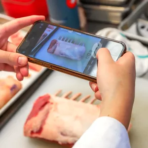 A student takes a photo of a cut of raw meat on their phone