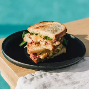 A grilled cheese sandwich with meat inside sits on a black plate on a wooden table