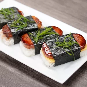 Four pieces of musubi sit on a white plate