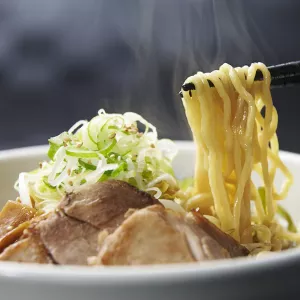 Chopsticks pull ramen noodles out of a bowl of soup