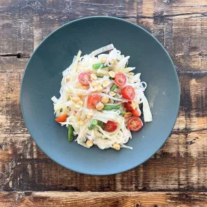 A bowl of fermented green papaya rice noodle salad on a wooden table