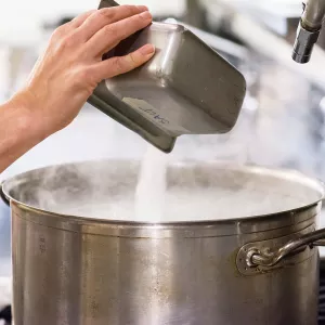 A chef pours salt into a steaming pot.
