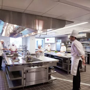 student in chef white practicing the sous-chef role while a chef-instructor looks on
