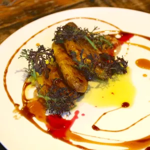 Sliced roasted yams sit on a white plate with colorful sauces and green herbs