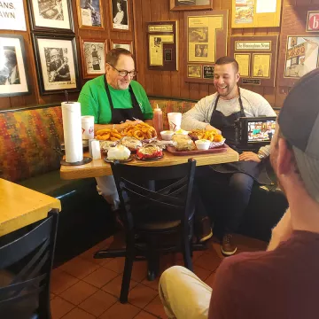 The show "Dom Eats Local" films a segment in a restaurant.