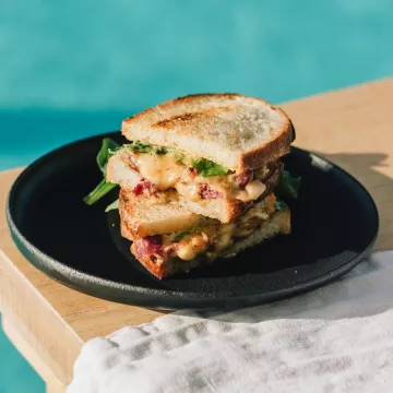 A grilled cheese sandwich with meat inside sits on a black plate on a wooden table