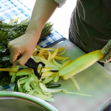 Chef peeling summer squash on a cutting board with herbs in the background