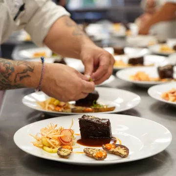 A student's hands plate a dish of meat, fingerling potatoes and cabbage salad on a white plate