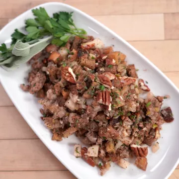 Stuffing sits on a white plate next to green herbs