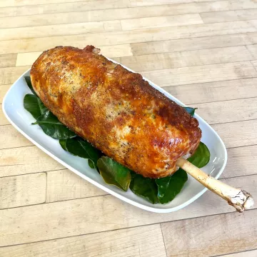 A large turkey roulade roast with a bone sticking out of the end sits on a white plate