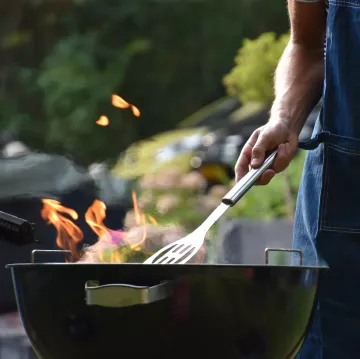 A person uses a spatula to cook outside on a fiery grill