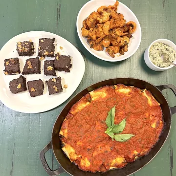 Vegan lasagna roll ups, buffalo cauliflower florets, pumpkin seed dip and brownies sit on a green table