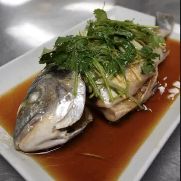 A whole steamed fish topped with green herbs on a white plate