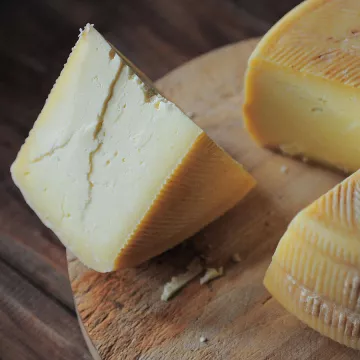 A piece of white cheese with a cheese rind on the outside sits on a piece of brown wood