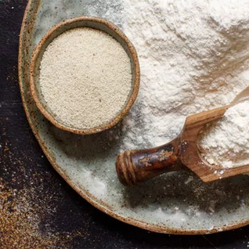 A bowl of uncooked fonio with a wooden scoop on top