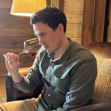 Sommelier Patrick Kaufman sits in a leather chair and smells a glass of red wine.
