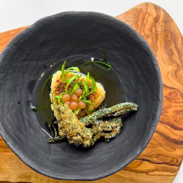 A piece of onigiri and multiple pieces of plant-based "salmon" skin sit on a blue plate