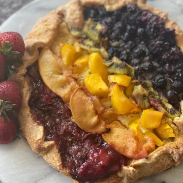 A galette filled with fruits of various colors to make a rainbow effect sits on a white plate