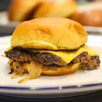 A cheeseburger with caramelized onions on a white plate