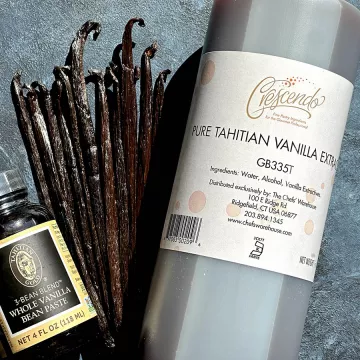 A bottle of Tahitian vanilla extract, raw vanilla beans and a small bottle of vanilla extract on a blue background