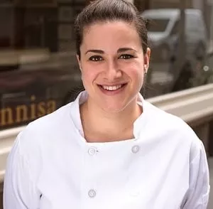 ICE graduate Mary Attea, a brunette woman in a white chef's coat, stands outside Annisa restaurant