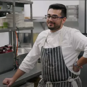 ICE alumni Chef Shant Halajian in a black and white stripped apron leans against the counter in a kitchen