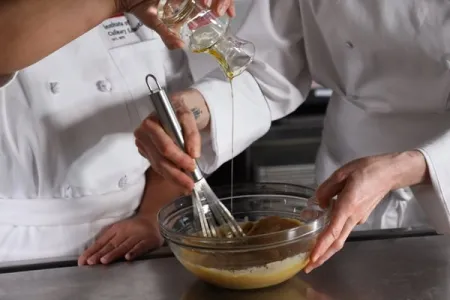 two Culinary Nutrition students add olive oil to emulsify a salad dressing