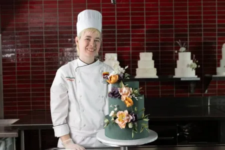 ICE Chef Chelsea Burgess in front of a cake with multi-colored gumpaste flowers from the ICE Professional Cake Decorating continuing education program