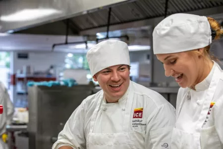 Two ICE students in chef's whites smile while working in class