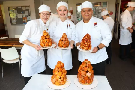 ICE students smile while holding croquembouche towers